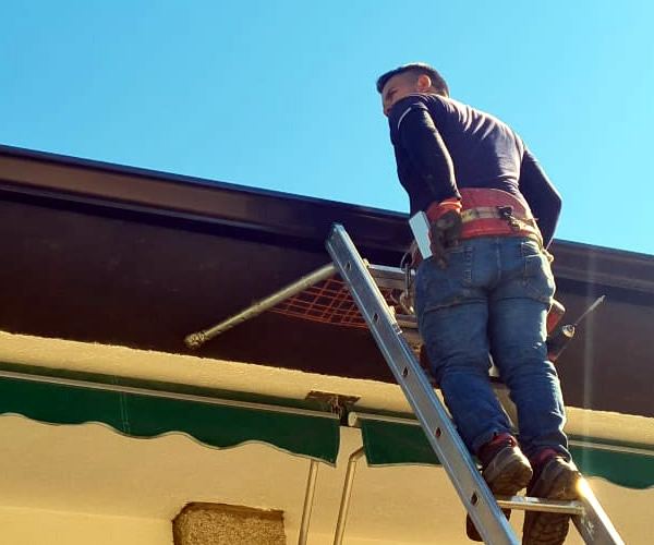 Operario limpiando un canalón desde escalera